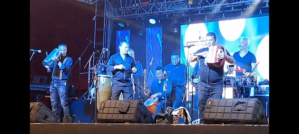 Grupo vallenato en tarima con acordeón, guacharaca, caja y congas, los músicos con camisa azul oscuro