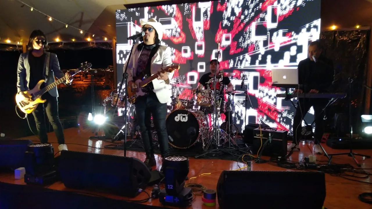 Mateo Acevedo y su banda completa tocan en vivo frente a una pantalla LED con una ciudad iluminada.