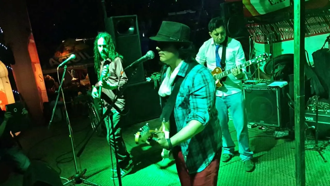 Mateo Acevedo con sombrero toca la guitarra junto a su banda bajo luces verdes en un club nocturno.