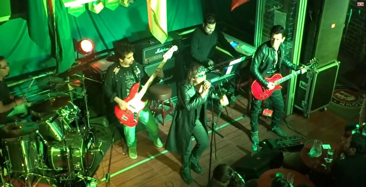 Mateo Acevedo cantando con su banda en vivo durante un concierto de rock en un bar con luces verdes.