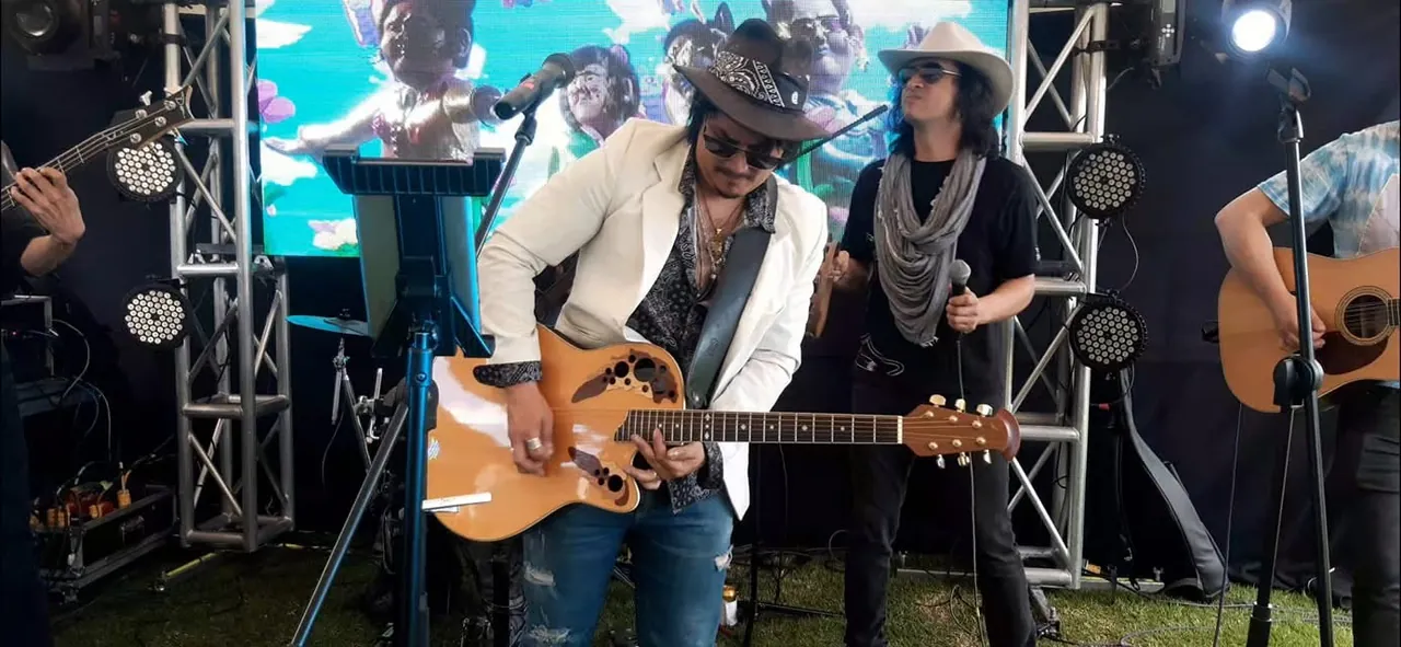 Mateo Acevedo toca la guitarra junto a su banda sobre una tarima con pantalla LED en una presentación en vivo.