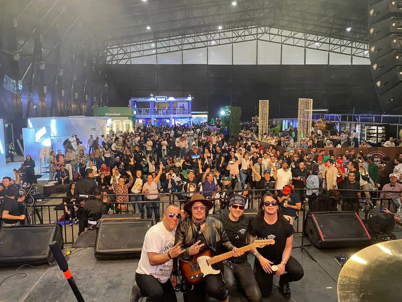 Mateo Acevedo y su banda posan en la tarima con el público de un concierto al fondo.