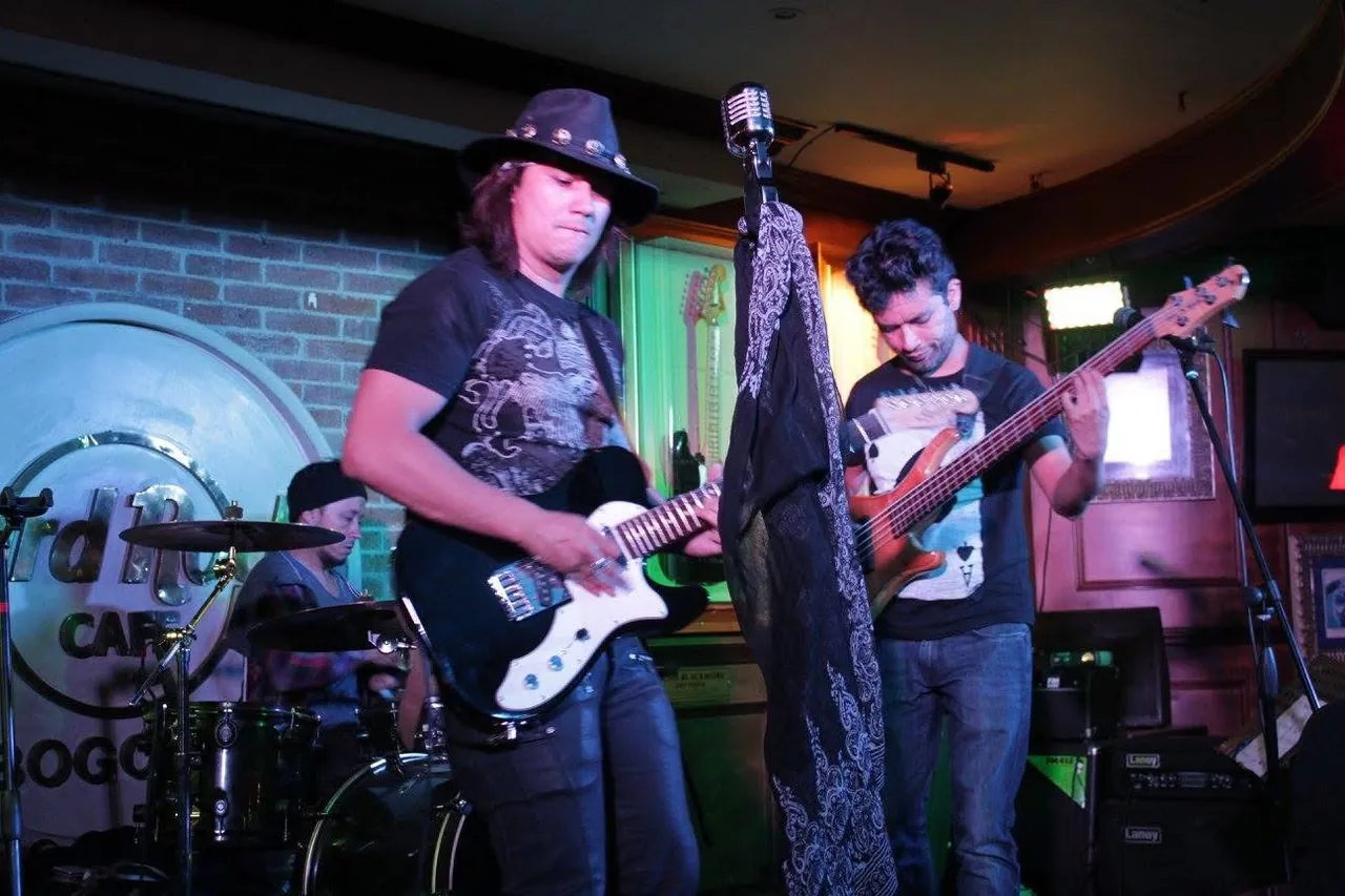 Mateo Acevedo con sombrero toca la guitarra junto a su banda en un bar de rock en Bogotá.