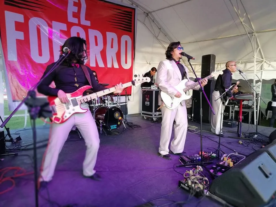 Mateo Acevedo y su banda con trajes claros y corbatines tocan en vivo bajo una carpa en un evento.
