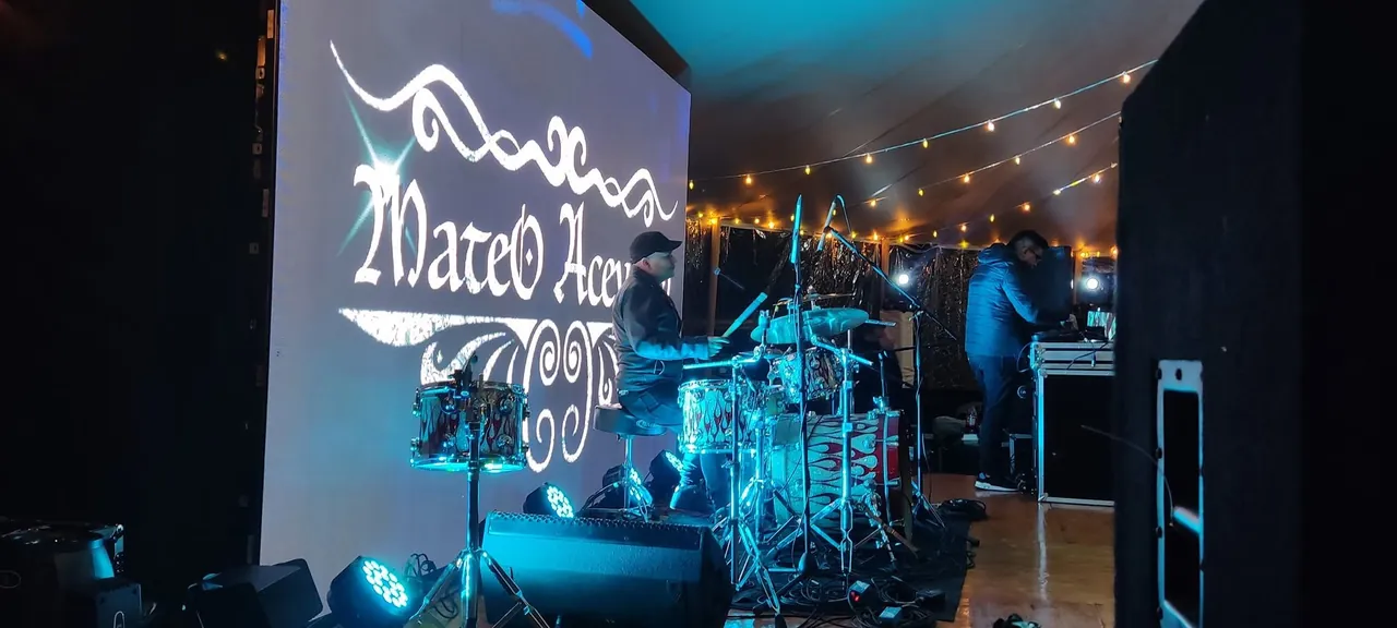 Batería en escena frente a la pantalla con el logo de Mateo Acevedo durante un show en vivo bajo carpa.