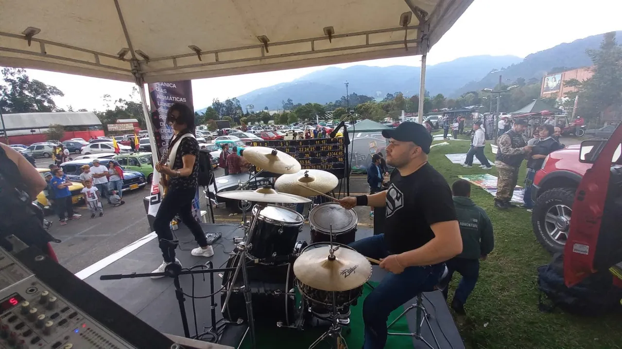 Baterista de la banda de Mateo Acevedo toca en un festival al aire libre con autos y montañas de fondo.