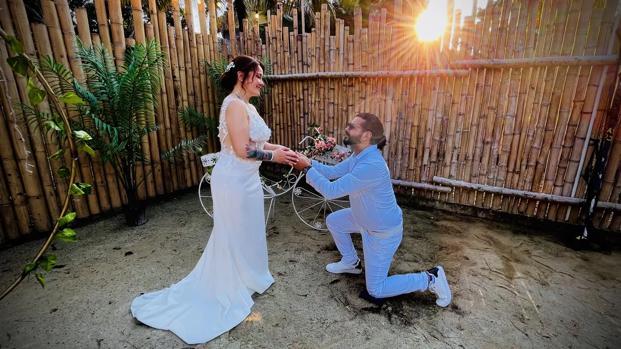 Momento romántico de una boda al atardecer, el novio arrodillado frente a la novia de vestido blanco.