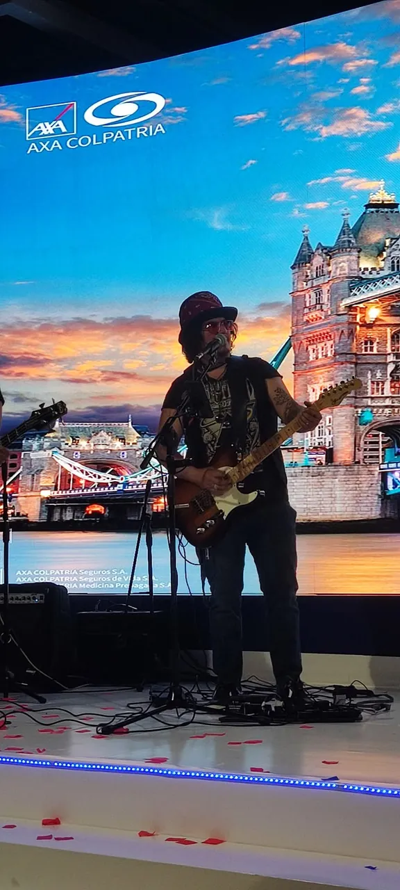 Mateo Acevedo canta y toca guitarra en un evento corporativo frente a una pantalla LED.