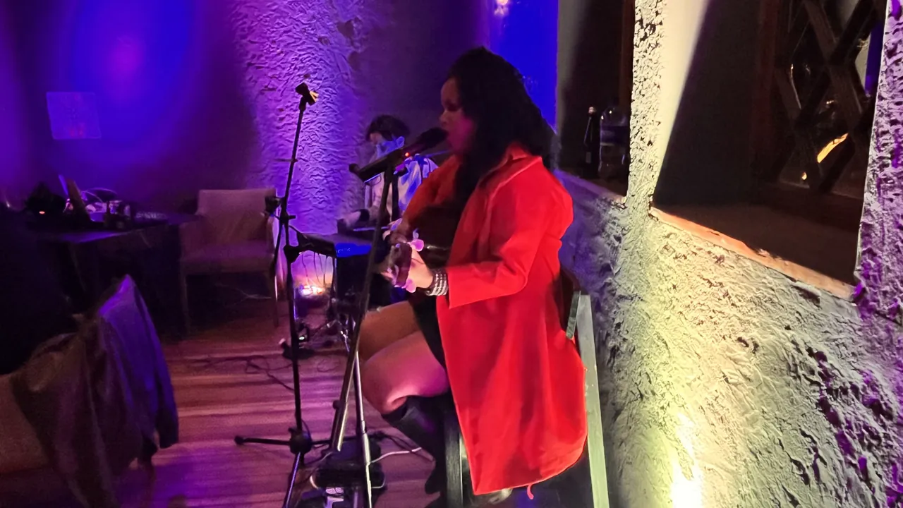 Cantante en vivo con saco rojo toca guitarra acústica en un evento íntimo.