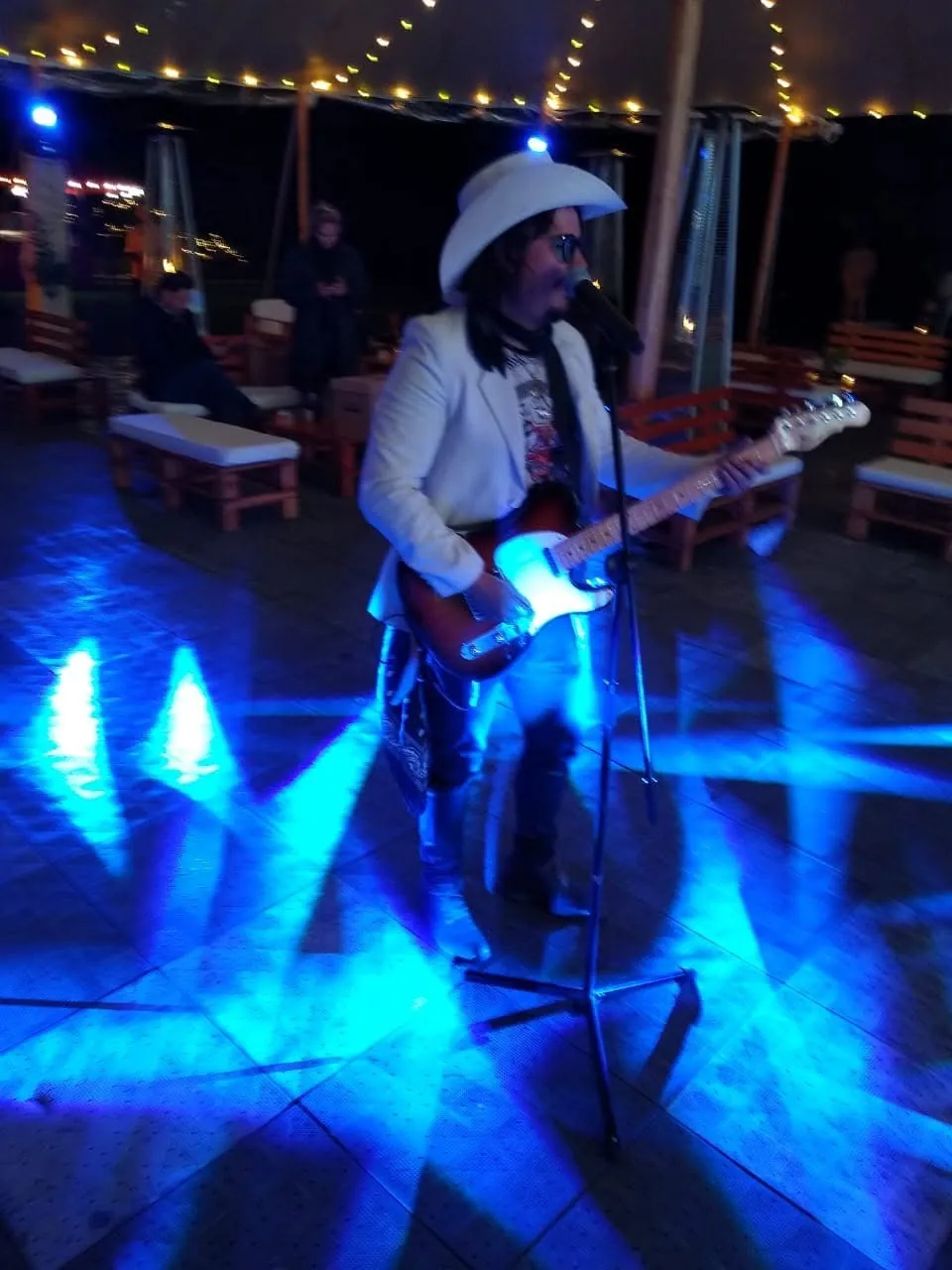 Mateo Acevedo canta y toca la guitarra bajo una intensa luz azul durante una presentación en vivo.