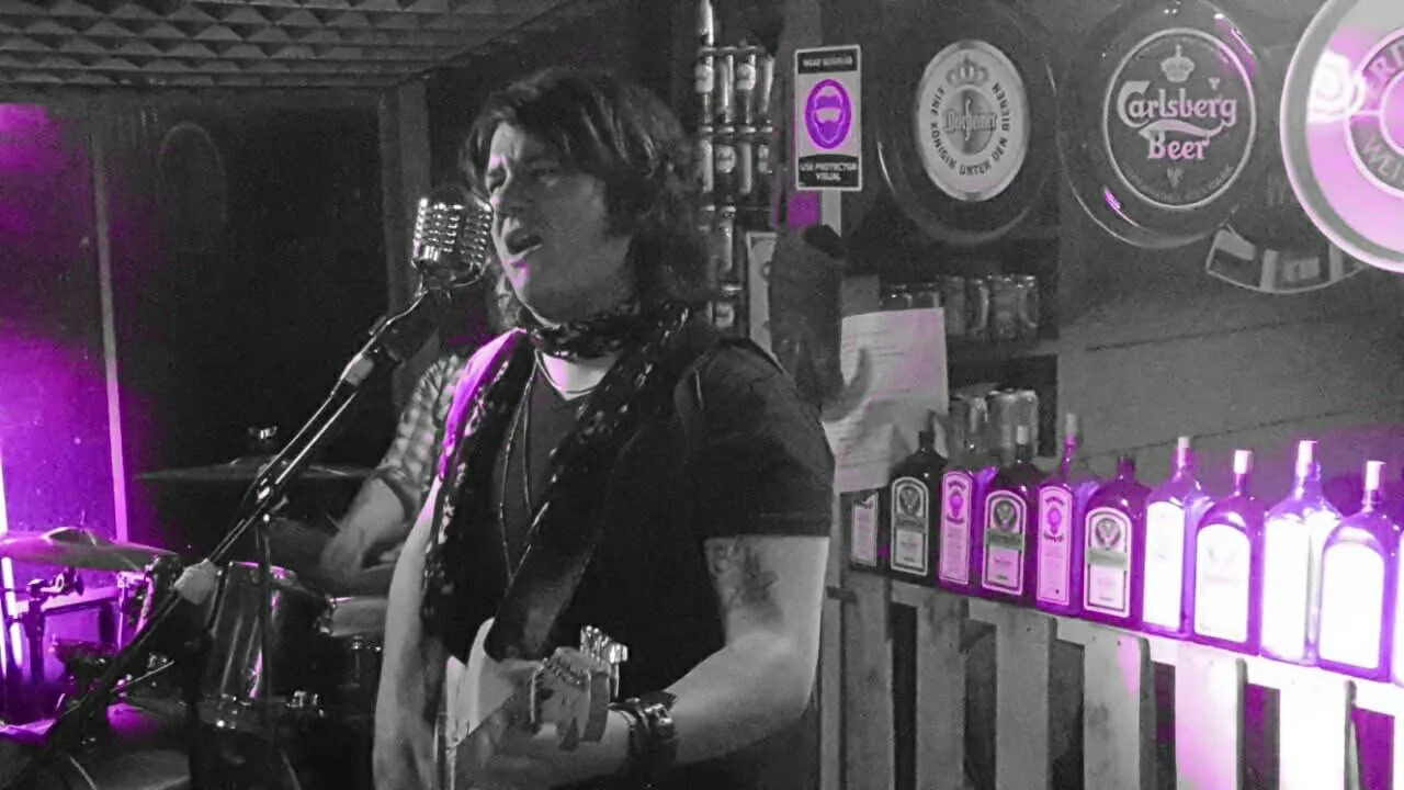 Mateo Acevedo canta y toca la guitarra en una presentación de rock en vivo dentro de un bar.