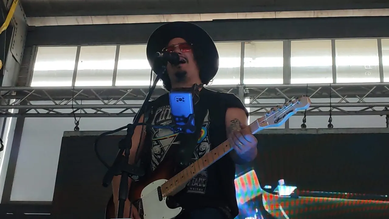 Primer plano de Mateo Acevedo cantando y tocando guitarra eléctrica en una presentación en vivo.
