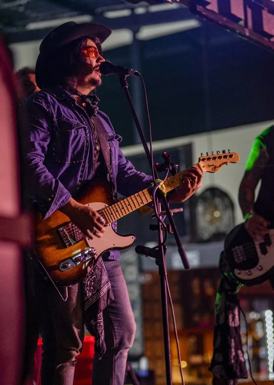 Mateo Acevedo canta y toca guitarra eléctrica con sombrero durante un show en vivo.