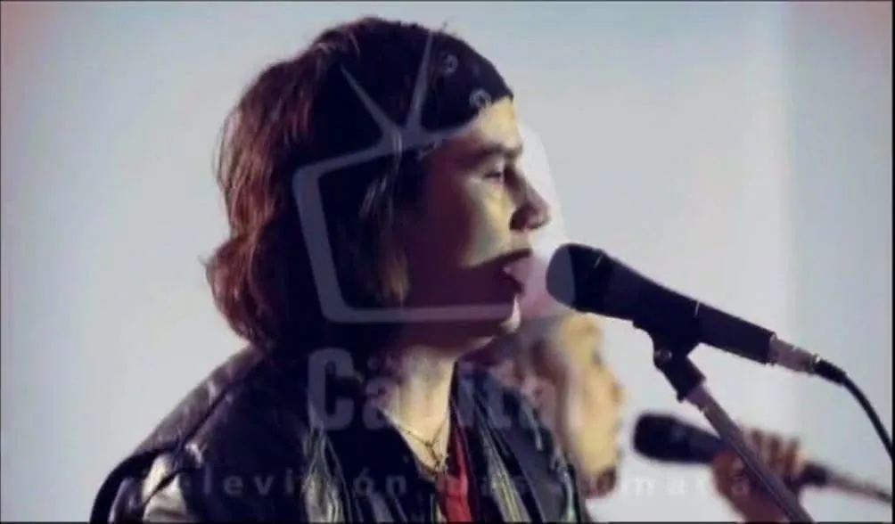 Retrato de perfil de Mateo Acevedo cantando al micrófono con chaqueta de cuero en una presentación en vivo.