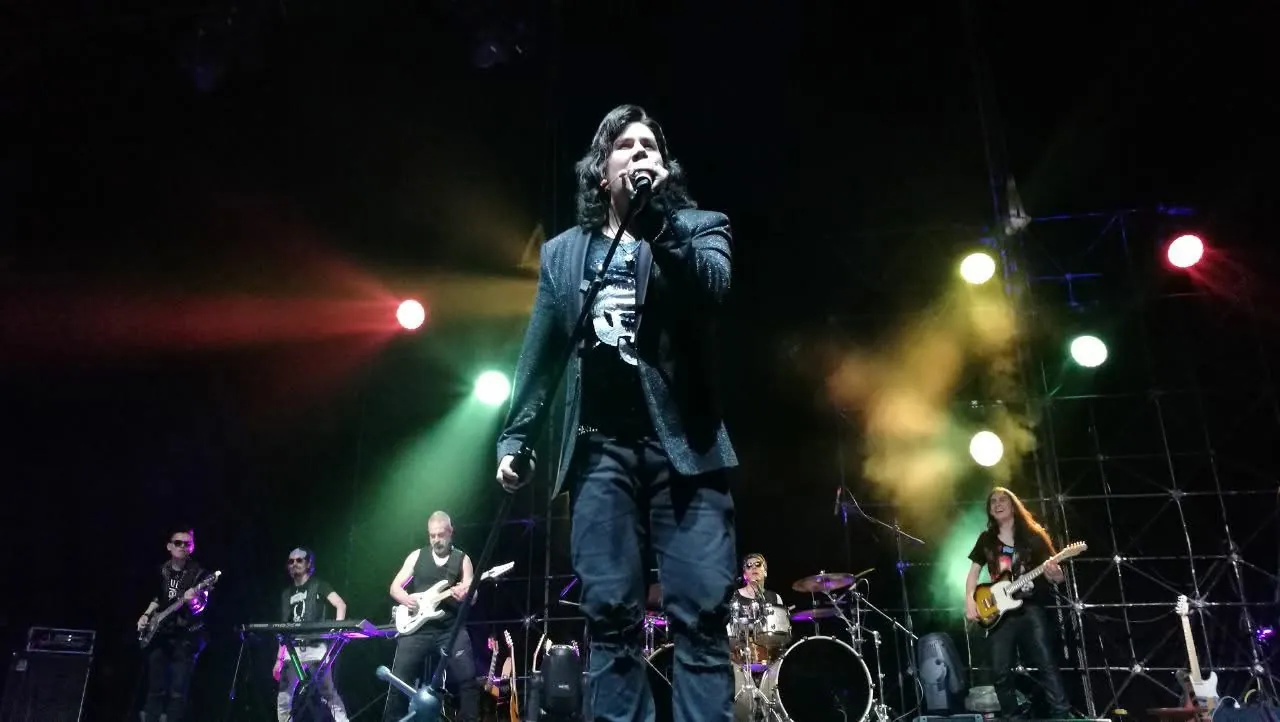 Mateo Acevedo canta al frente de su banda completa durante un concierto de rock en vivo sobre una gran tarima.