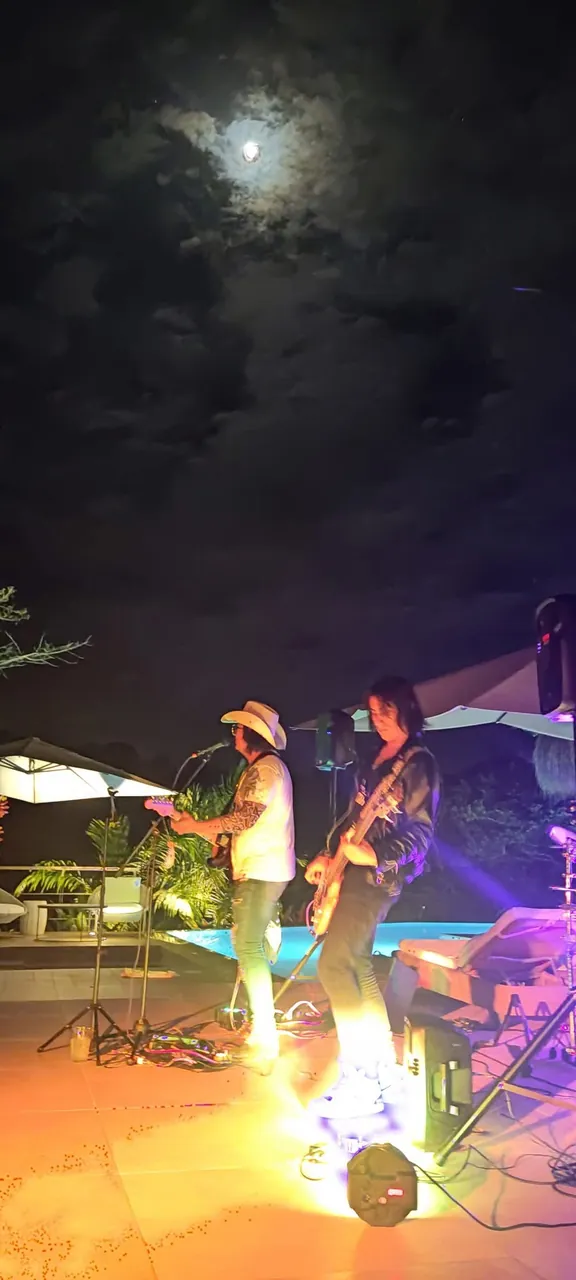 Mateo Acevedo toca la guitarra y canta en un concierto nocturno junto a una piscina bajo la luna llena.