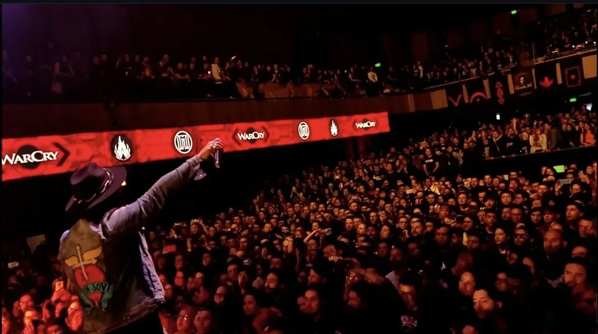Mateo Acevedo frente a un público masivo en un concierto, con el micrófono en alto.