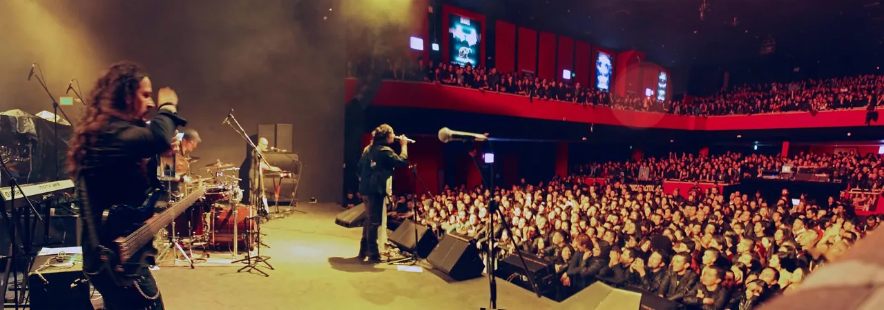 Mateo Acevedo canta al micrófono ante una enorme multitud en un concierto dentro de un teatro.