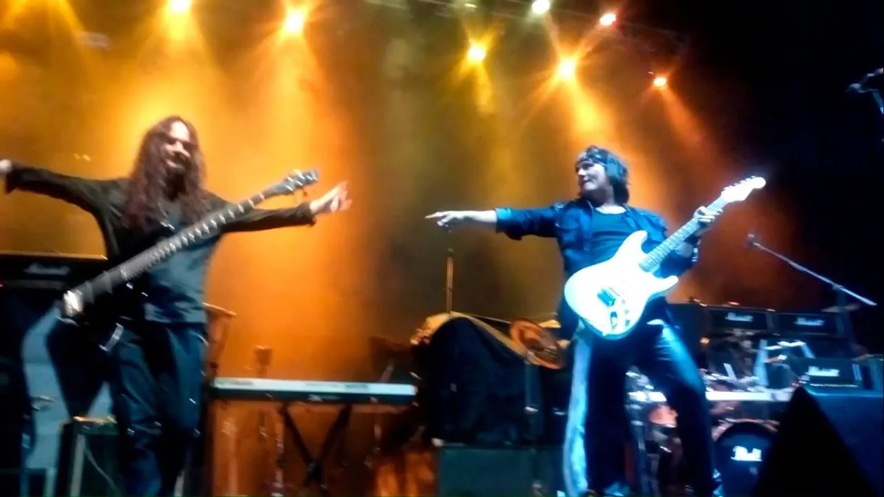 Mateo Acevedo con su guitarra blanca señala a otro guitarrista de la banda en un concierto en vivo.