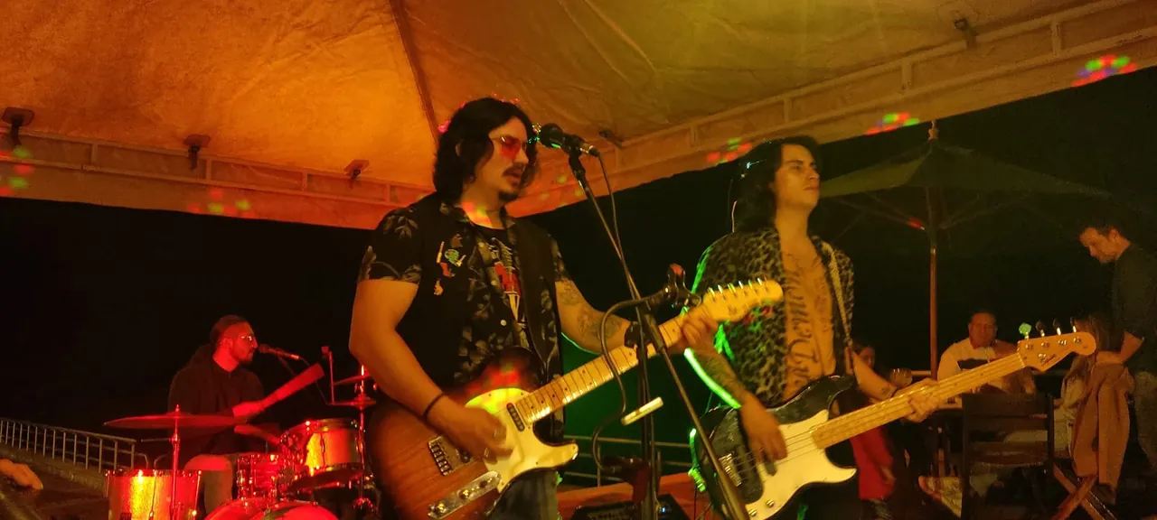 Mateo Acevedo toca la guitarra junto a otro músico durante un evento en vivo bajo carpa.