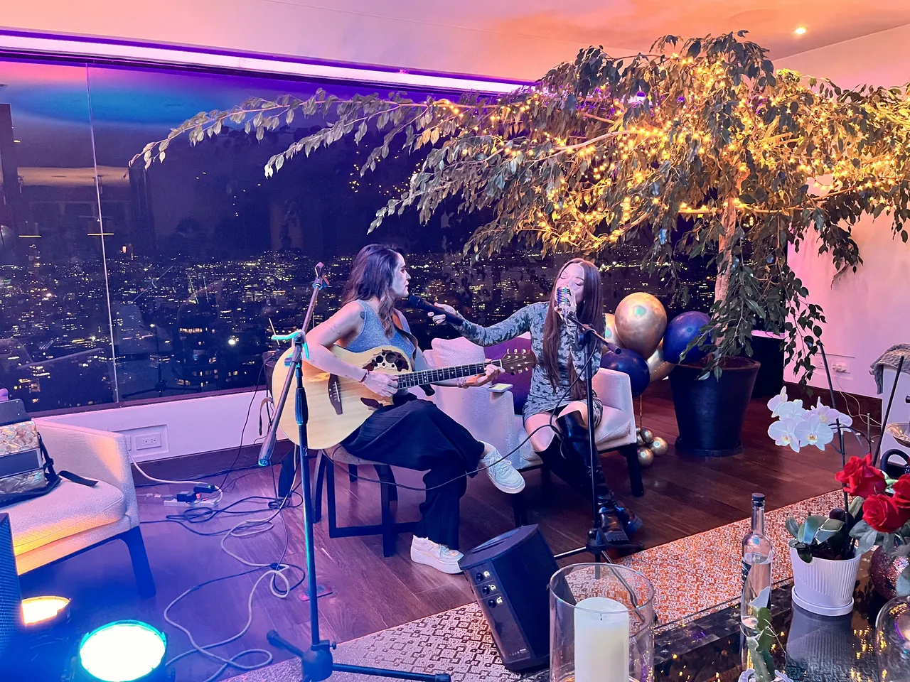 Dúo acústico cantando en una terraza con vista nocturna de Bogotá durante una celebración privada.