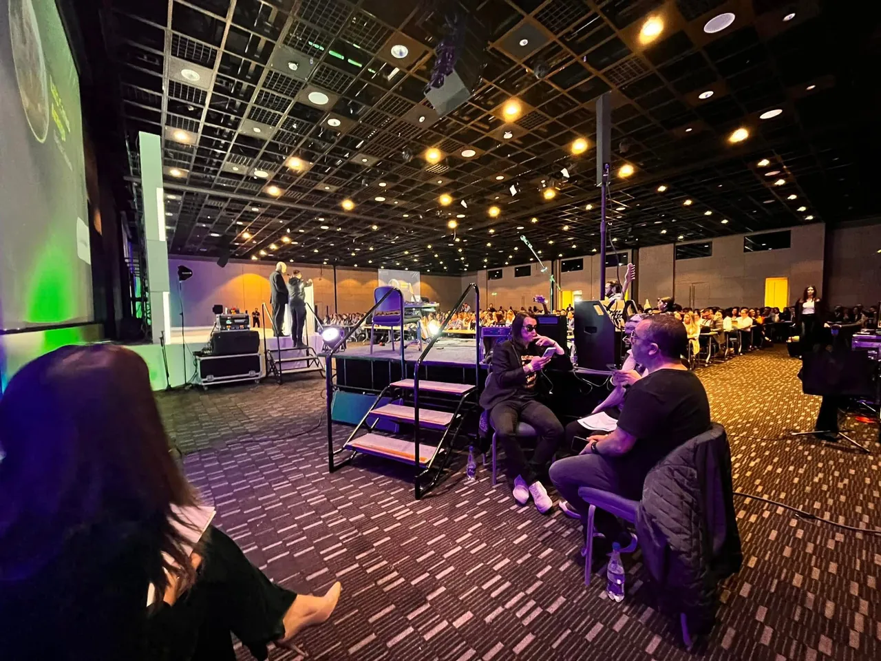 Tarima montada para un evento corporativo en un salón con asistentes e iluminación de colores.