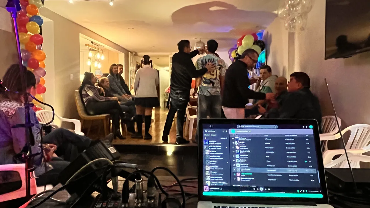 Equipo de música en vivo con laptop y software de audio durante un evento social mientras los invitados comparten.