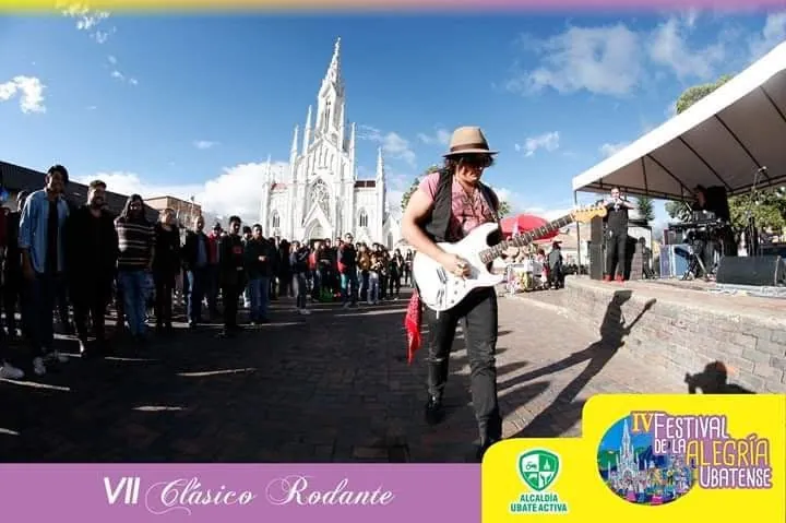 Mateo Acevedo tocando guitarra eléctrica en un festival al aire libre, en la plaza frente a una catedral.