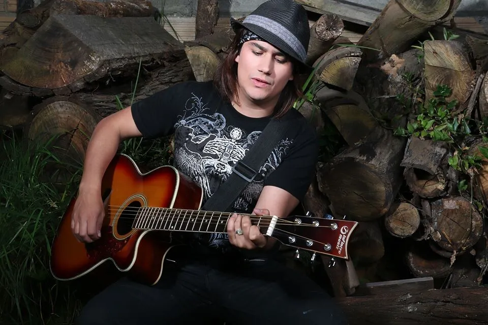 Mateo Acevedo joven tocando guitarra acústica entre troncos de madera