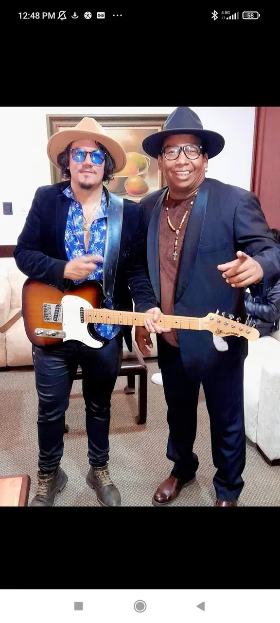Mateo Acevedo posa con una guitarra eléctrica junto a un invitado en un retrato entre bastidores.