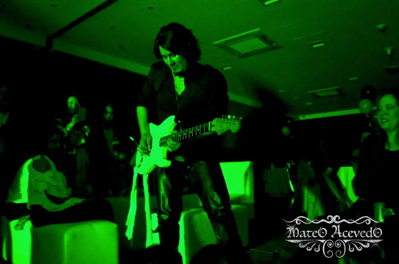 Mateo Acevedo toca la guitarra eléctrica en un evento social iluminado de verde, rodeado por los asistentes.