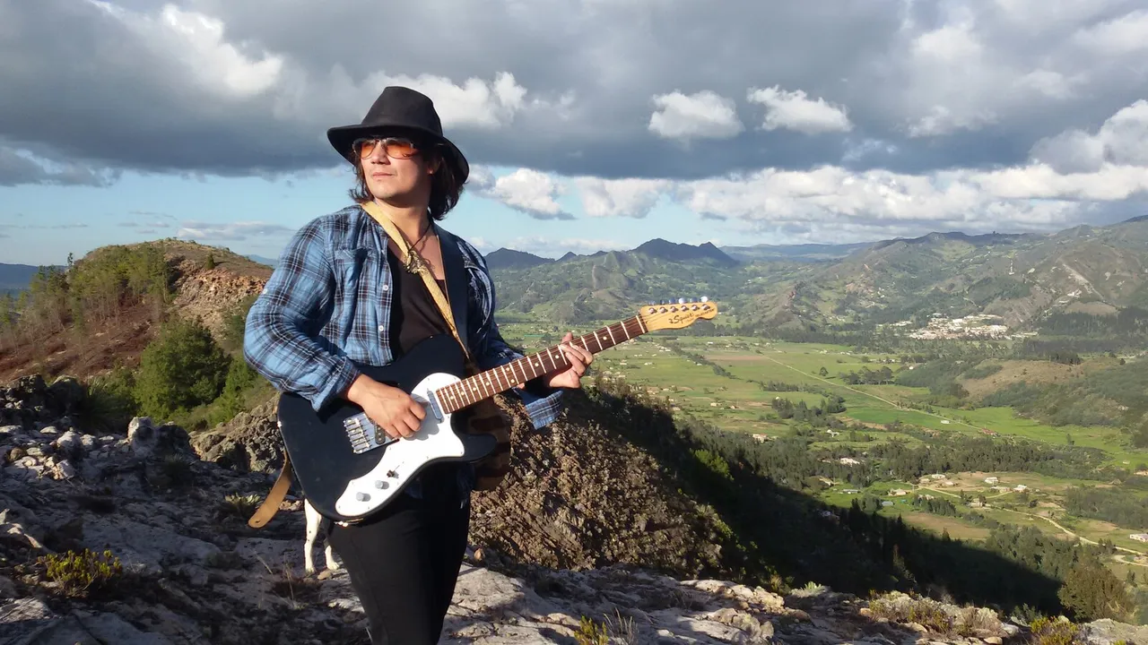 Mateo Acevedo tocando guitarra eléctrica sobre una roca con paisaje de montañas