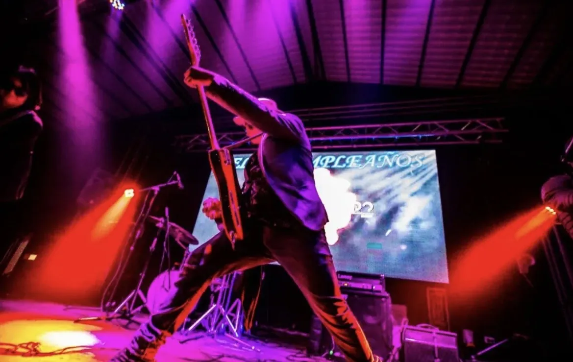Mateo Acevedo levanta su guitarra eléctrica en una pose de rock durante un show en vivo.
