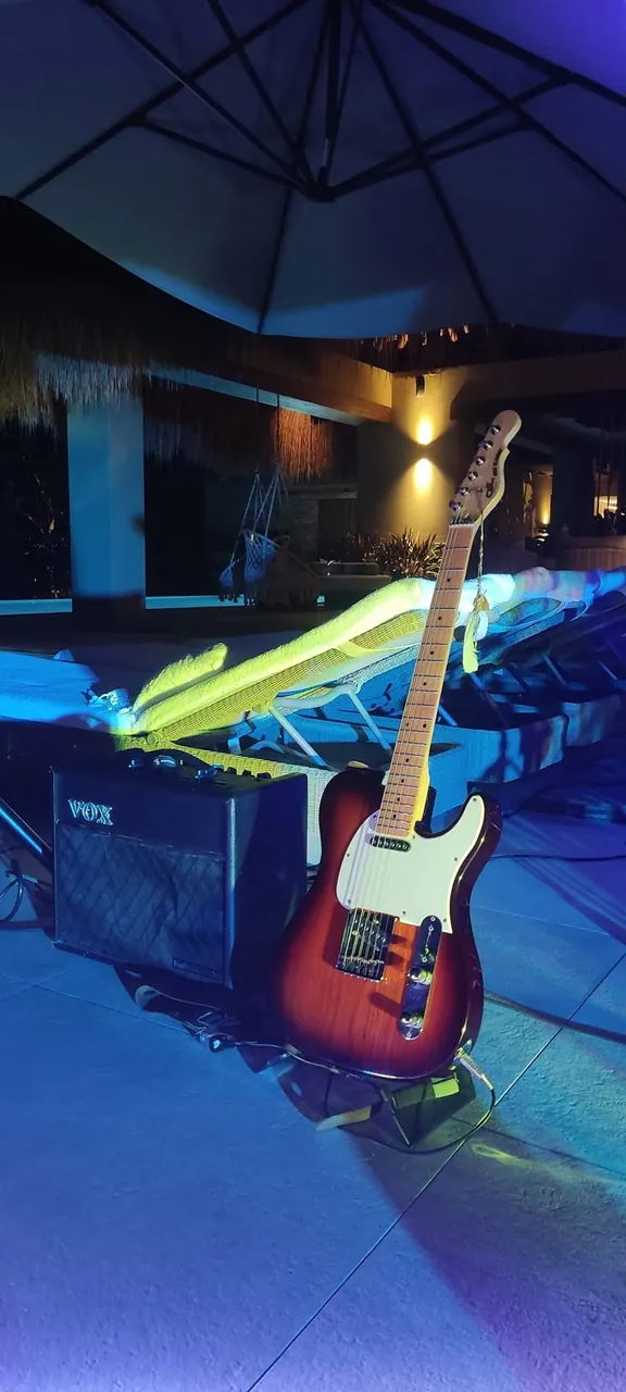 Guitarra eléctrica Telecaster sunburst apoyada en un amplificador, lista para un evento nocturno al aire libre.