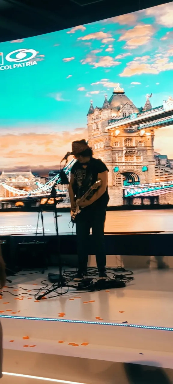 Mateo Acevedo concentrado tocando la guitarra en un evento empresarial con pantalla LED.