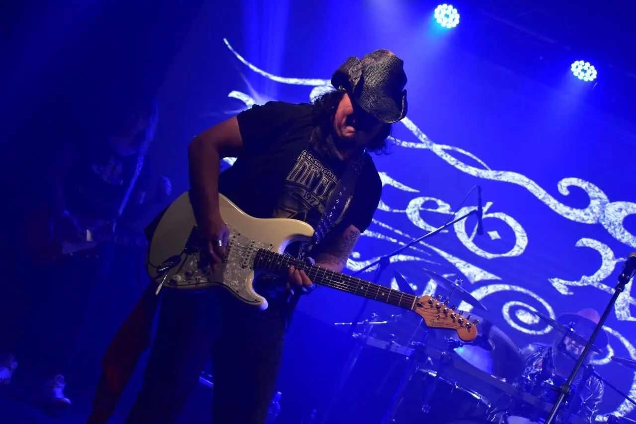 Mateo Acevedo toca la guitarra eléctrica bajo luces azules durante un concierto en vivo.
