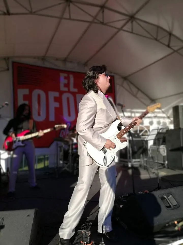 Mateo Acevedo toca la guitarra eléctrica vestido de traje claro durante una presentación en vivo bajo una carpa.