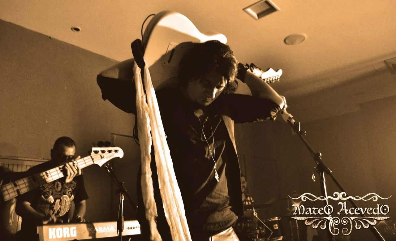 Mateo Acevedo levanta su guitarra en pleno show de rock en vivo junto al bajista, en tono sepia.