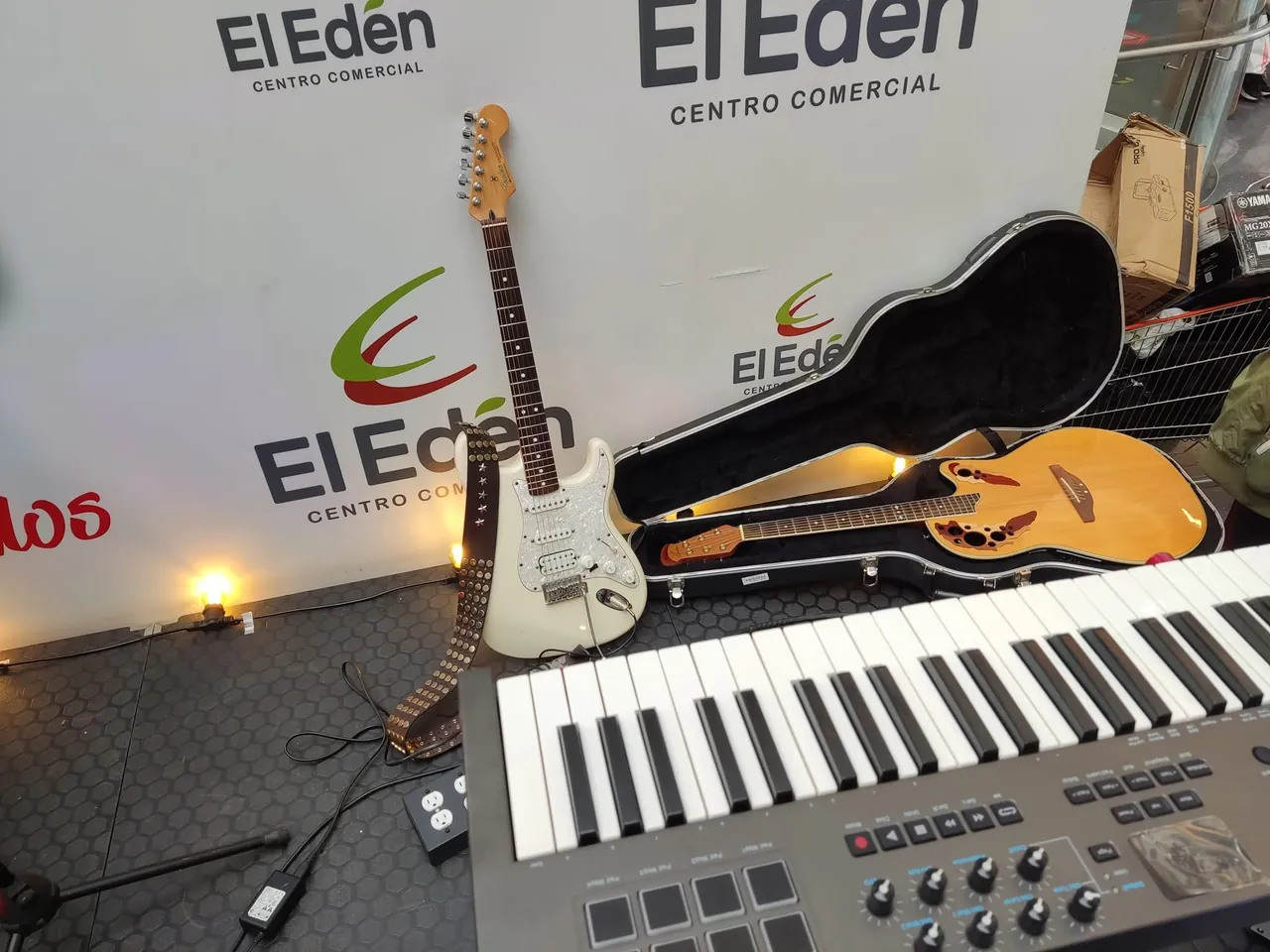 Guitarra eléctrica, guitarra acústica y teclado dispuestos en el escenario antes de un evento en vivo.