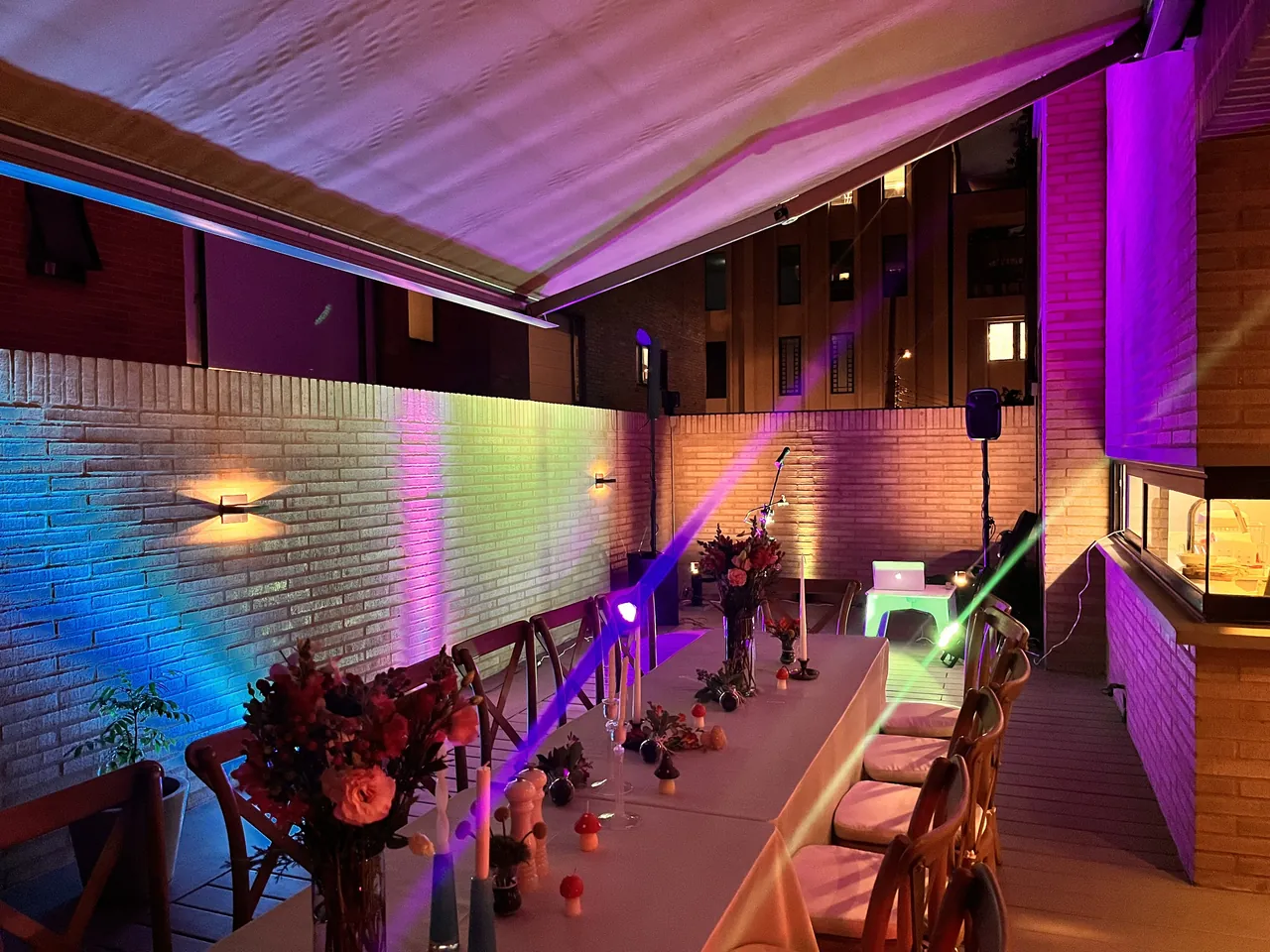 Montaje de un evento social en una terraza con mesa larga decorada, centros florales y luces de colores.