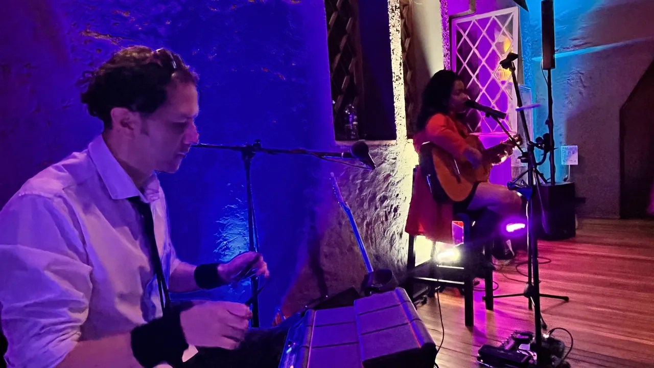 Músicos en vivo durante un evento íntimo con guitarra acústica e iluminación azul.