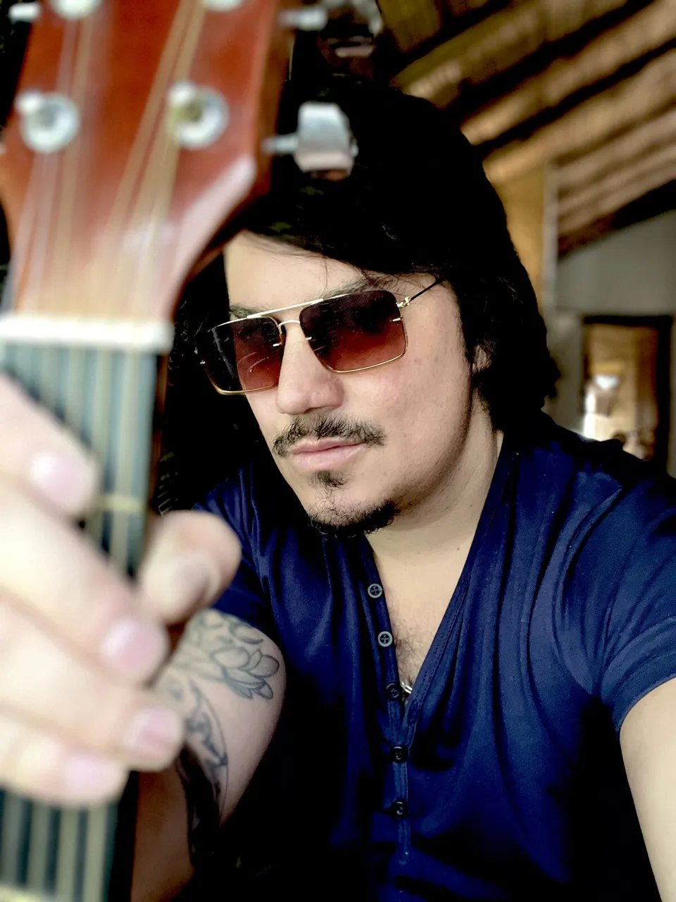 Mateo Acevedo con gafas de sol extendiendo el brazo junto a su guitarra