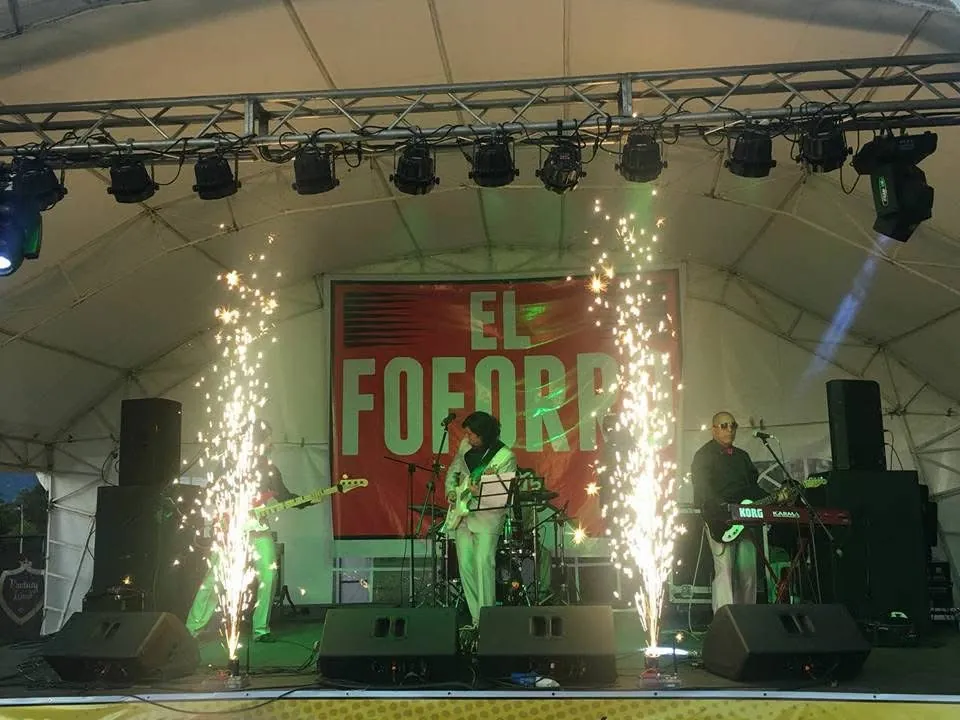 Tarima con chispas pirotécnicas durante una presentación en vivo de la banda bajo una carpa en un festival.