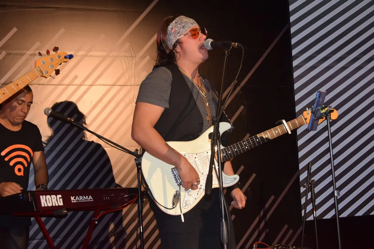 Mateo Acevedo cantando frente al micrófono y tocando guitarra eléctrica en una presentación en vivo.