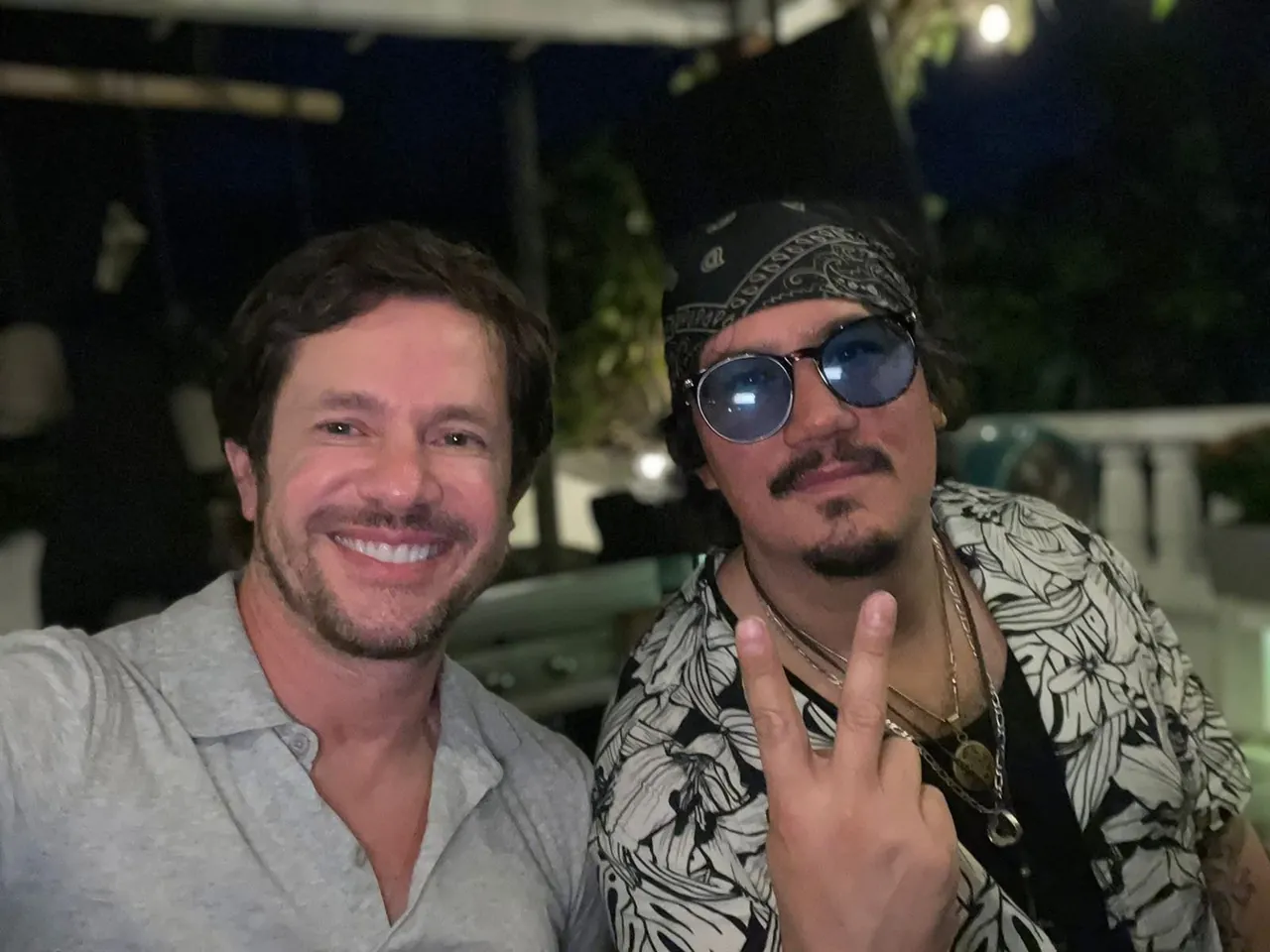 Retrato nocturno de Mateo Acevedo junto a un invitado en un evento, con su característico estilo rockero.
