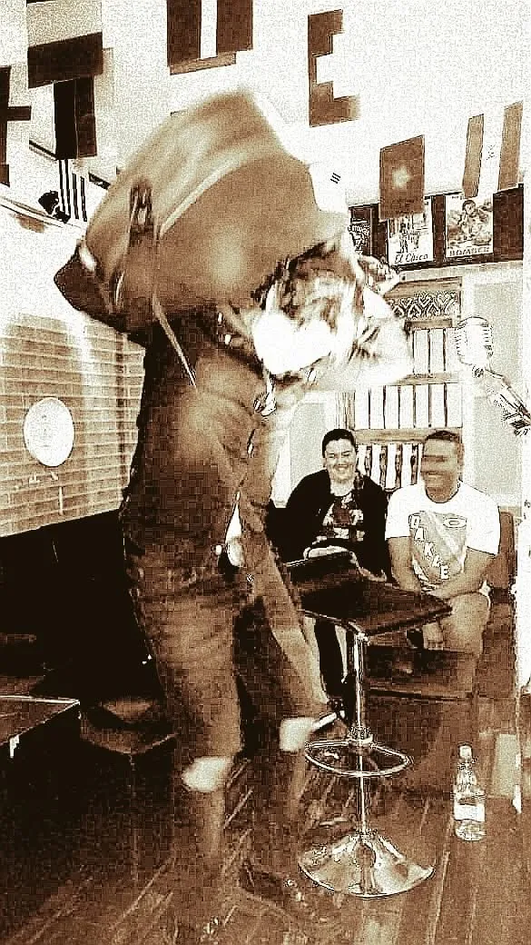 Mateo Acevedo en una presentación íntima en vivo con tono sepia, ante un pequeño público sentado.