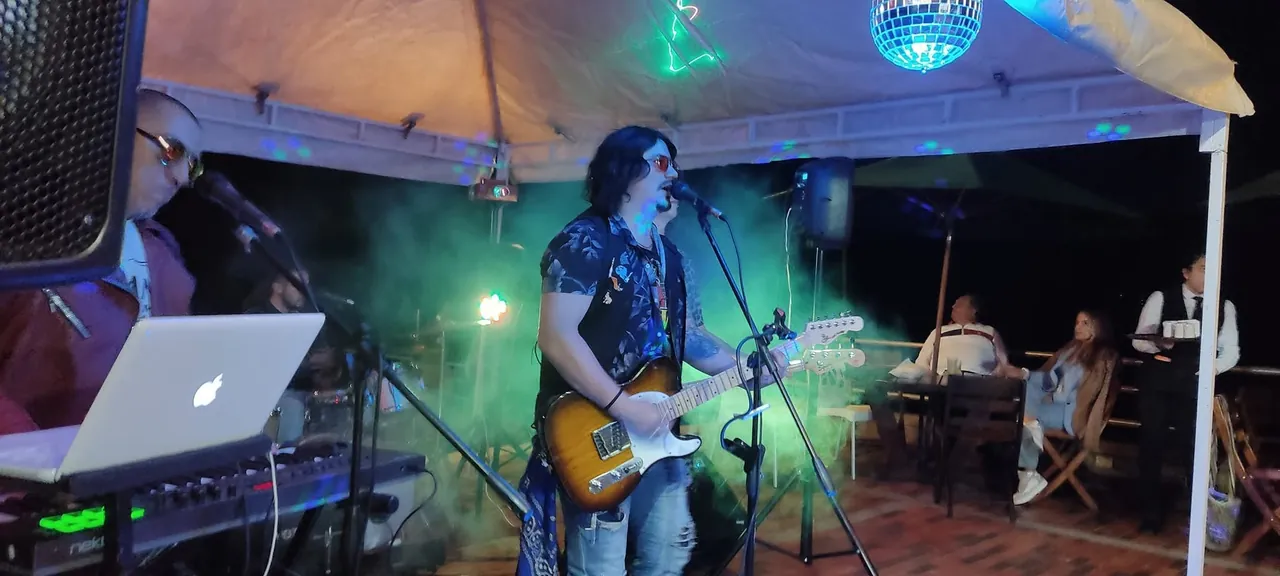 Mateo Acevedo canta y toca guitarra bajo una carpa con bola de espejos en un evento social.