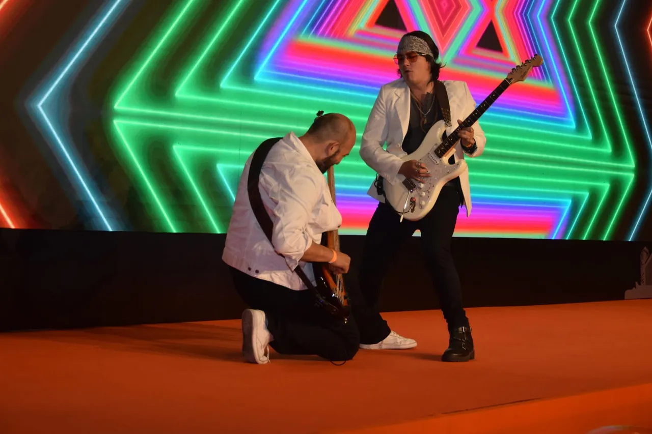 Mateo Acevedo tocando guitarra en un show en vivo sobre tarima con pantalla LED de neón durante un evento.