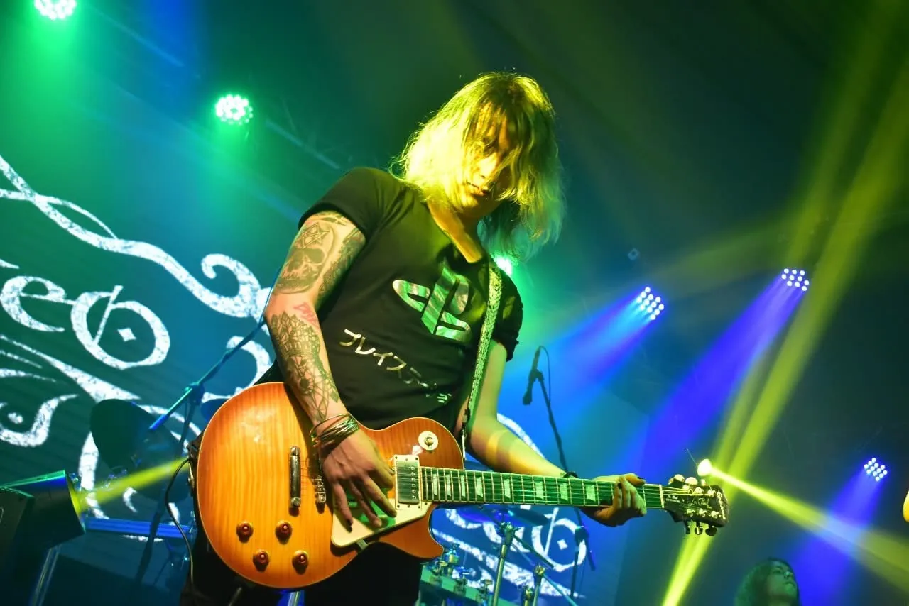 Mateo Acevedo interpreta la guitarra eléctrica durante un show de rock con iluminación de escenario.