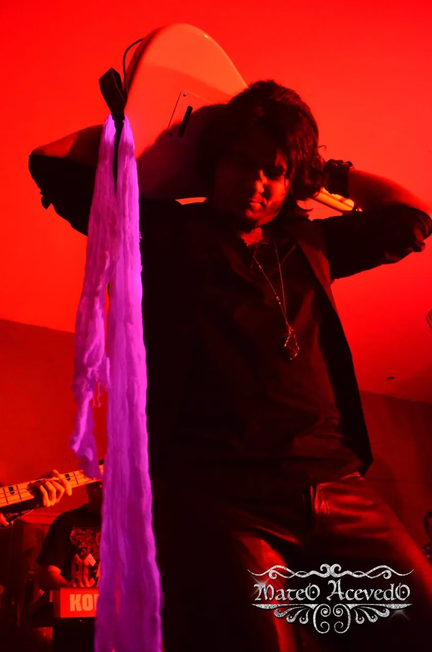 Mateo Acevedo en una pose intensa sobre la tarima durante un show de rock en vivo con luz roja.